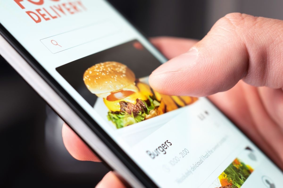 Close-up photo of someone looking at a burger on a food delivery app on their phone.
