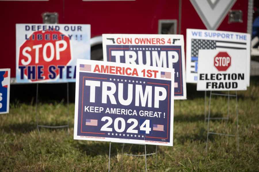 Several pro-Trump yard signs are displayed in the grass, printed with slogans like “Gun Owners 4 Trump,” “Defend Our Liberty,” and “Stop Election Fraud.”