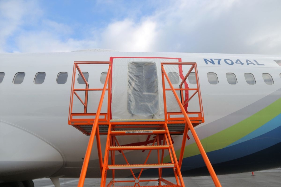 An orange metal platform stands in front of a plastic-covered hole in the side of a plane.