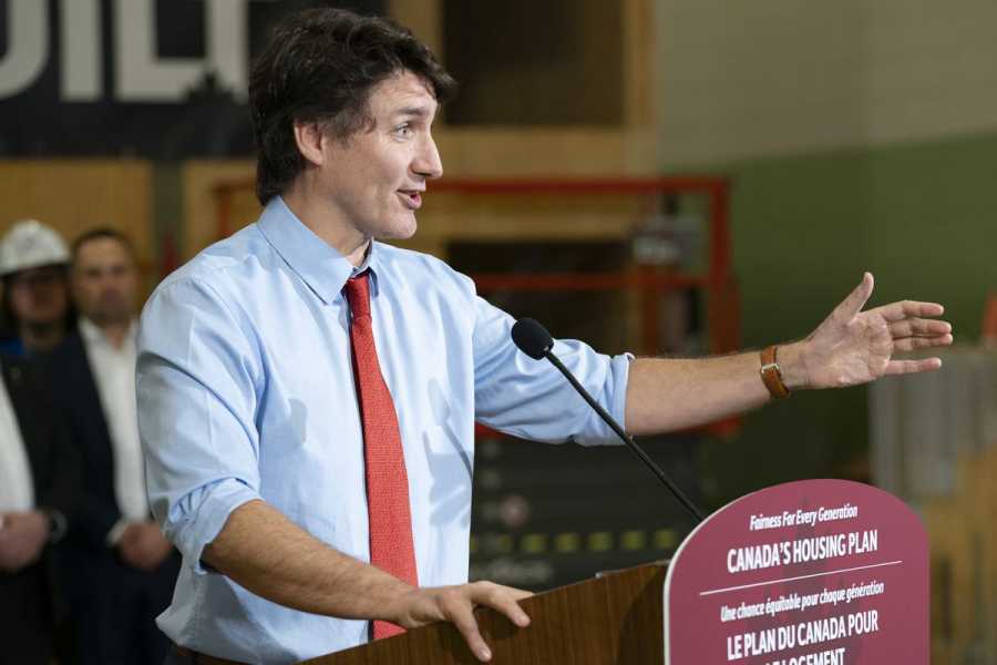 Trudeau, in a blue shirt with rolled-up sleeves, gestures widely as he speaks at a podium before a crowd.