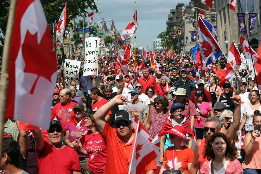 A mass of people wearing red and holding signs  and Canadian flags flood a city street.