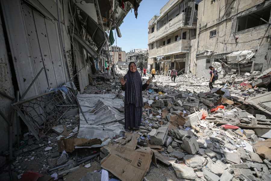 A Palestinian woman stands amid rubble, her arms  turned upward and a sad expression on her face, in the remains of a city street in Gaza.