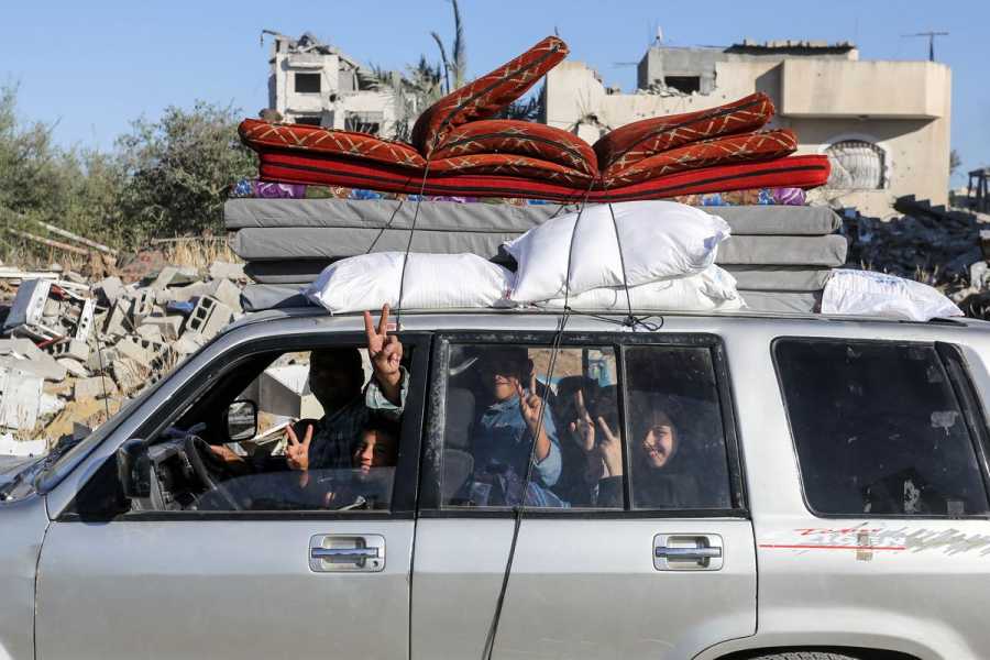 Palestinians in a packed car with mattresses stacked on top.