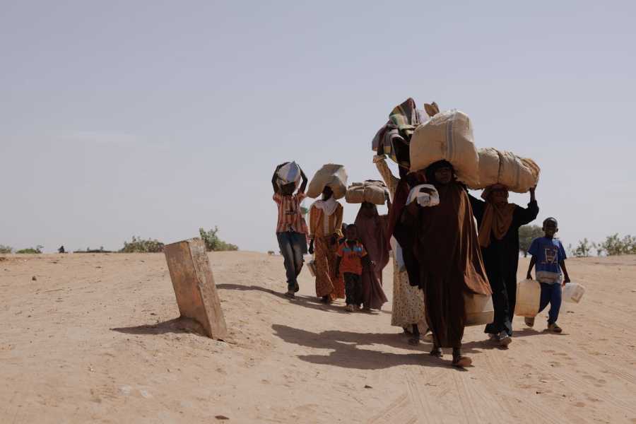 A group of people walking through a desert landscape while carrying their possessions on their heads.