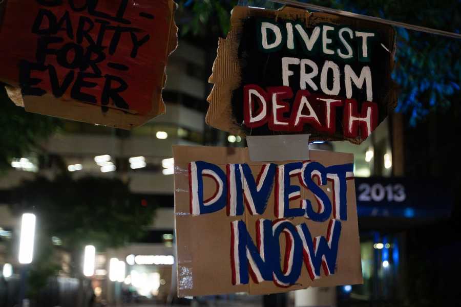 Two signs, one reading “Divest from death,” the other “Divest now.”