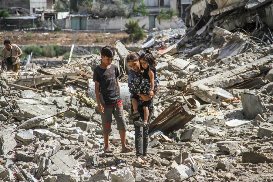 Palestinian kids walk over the rubble of a building