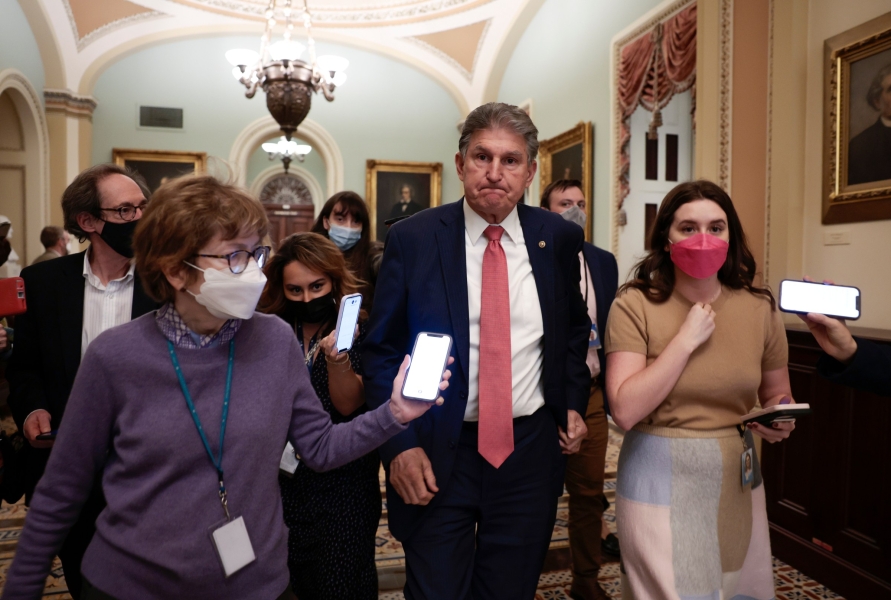 Manchin walks in a Capitol hallway flanked by masked reporters and aides on December 17, 2021.